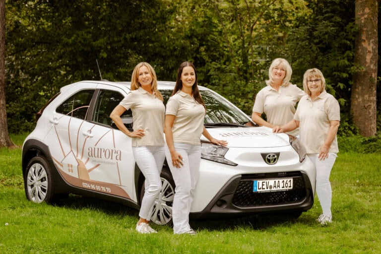 Das Team vom ambulanten Pflegedienst aurora in Leverkusen vor einem der Autos im Grünen